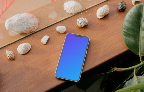 iPhone 13 Pro mockup em uma mesa de madeira ao lado de conchas do mar