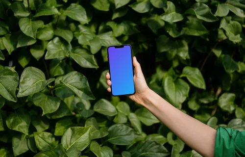 Woman holding an iPhone 13 mockup in front of green leaves