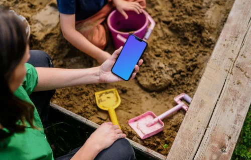 Woman holding an iPhone 13 mockup in sandpit