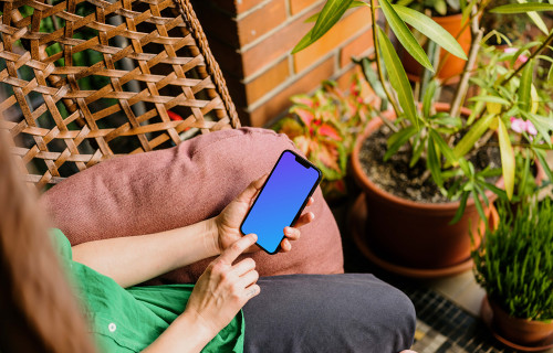 Woman typing on an iPhone 13 mockup in garden