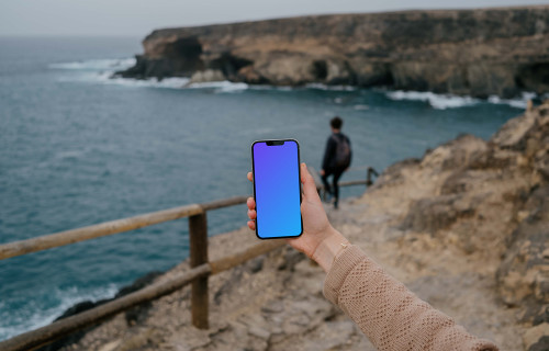 iPhone 13 Pro mockup segurado por um usuário em um litoral
