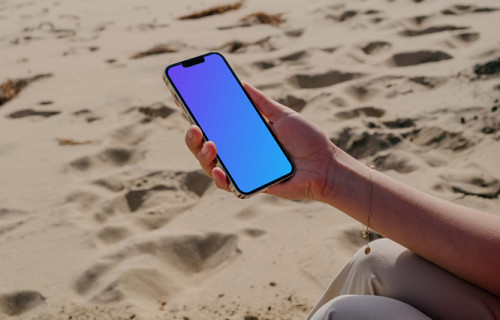 iPhone 13 Pro mockup segurado por um usuário sentado na areia da praia