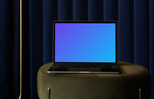 MacBook mockup em um banco de sofá com cortina azul no fundo