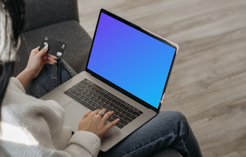 Mockup de usuário feminino em um sofá de compras on-line com seu MacBook cinza e um MasterCard na mão