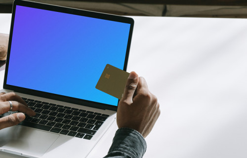 Usuário de MacBook com um cartão de débito em mãos mockup.